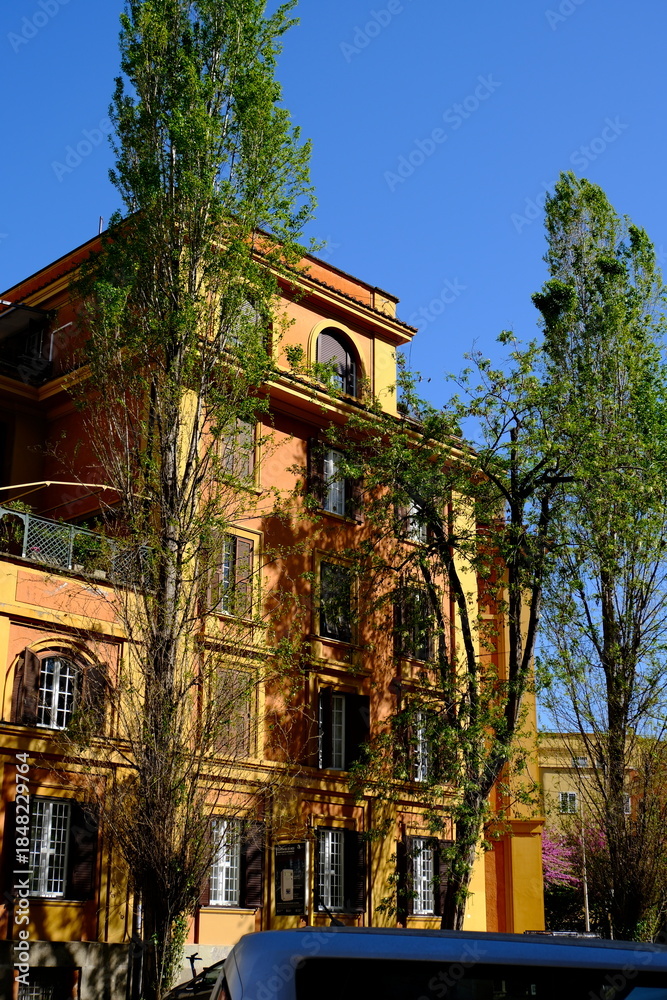 Obraz premium Urban building painted in orange and yellow tones with trees against a clear blue sky
