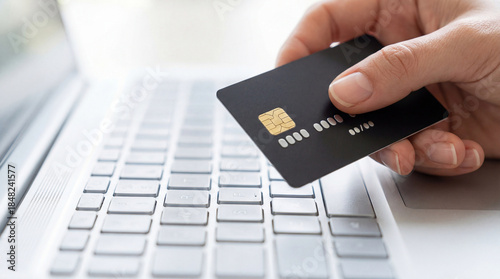 Hand holding black credit card for online shopping payment on laptop computer, technology in e-commerce banking