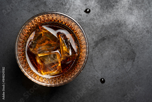 whiskey on the rocks in a glass placed on a dark textured surface