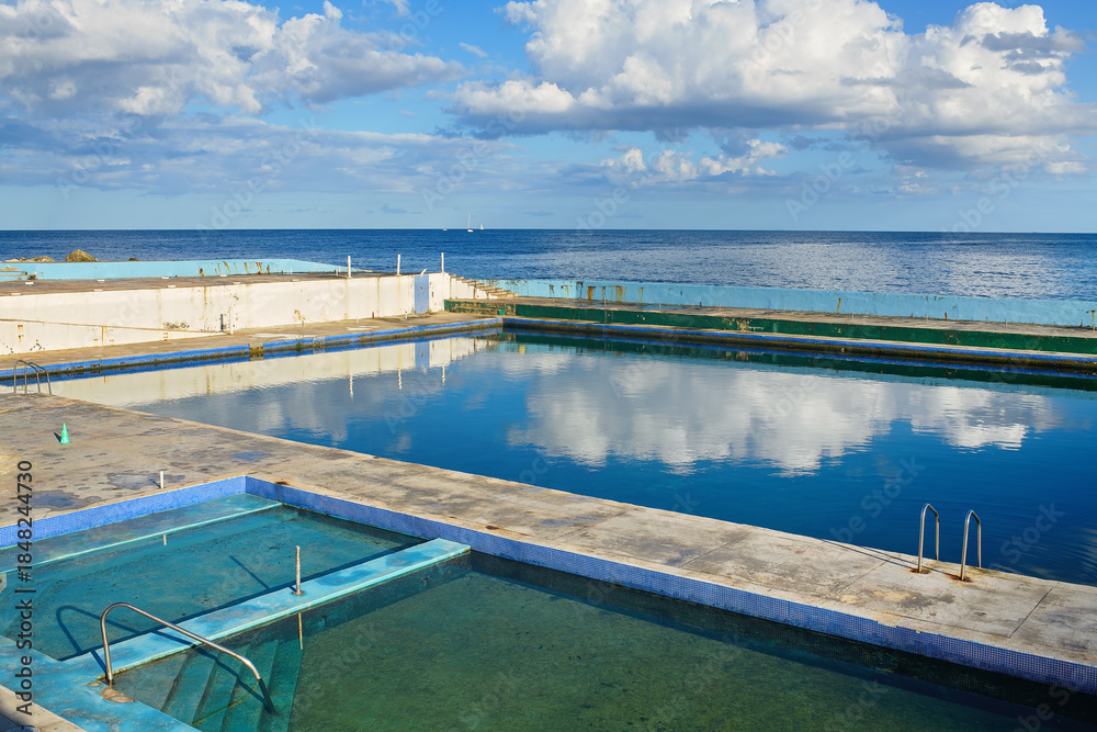Fototapeta premium Outdoor seawater training pools for a diving school reflecting a cloudy blue sky by the sea, used for scuba diver education and water sports activities.