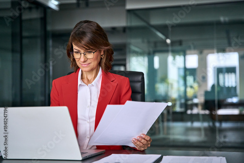 Focused latin business woman accountant working on laptop computer reading financial contract document in office workplace. Mature manager businesswoman specialist doing paperwork using pc. Copy space