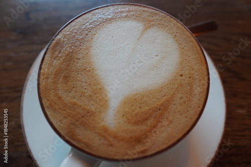 Warm coffee with heart design served in a cup on a wooden table in a cozy cafe setting