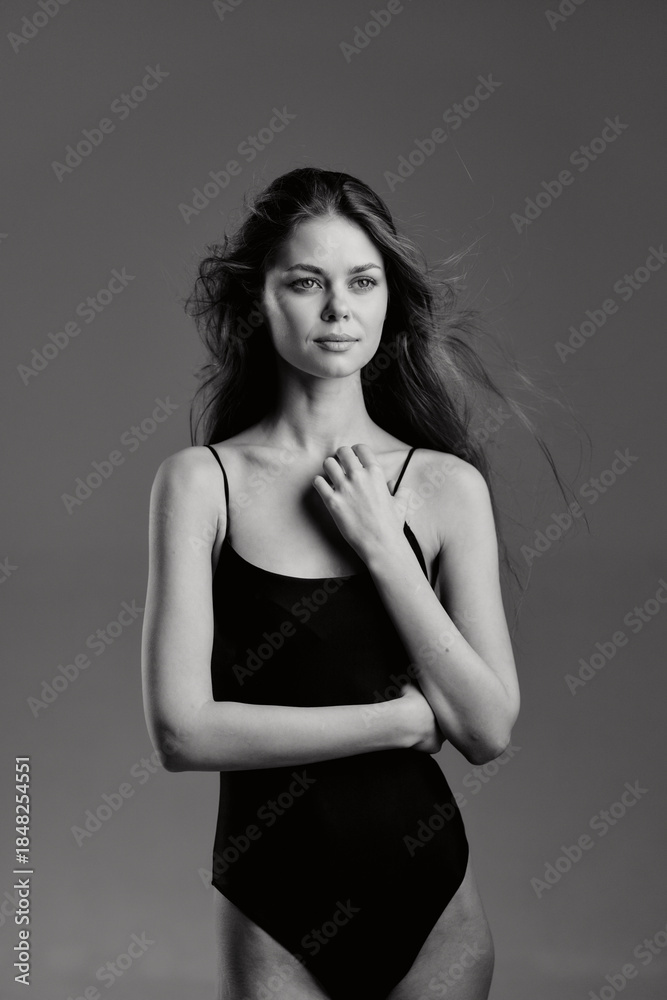 Fototapeta premium Black and white portrait of a young woman in a simple black bodysuit with calm expression and windblown hair.
