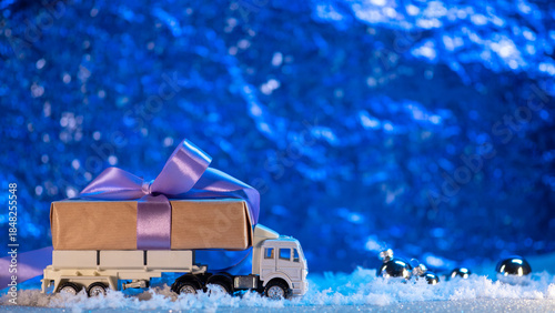 A Christmas truck is transporting a gift box, a snowy blue background with copy space. Delivery concept