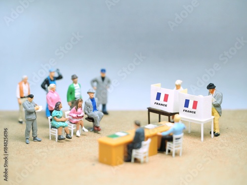 View of many miniature people at table. Background is blurred. Election day conceptual design with mini toy figure and France flag.