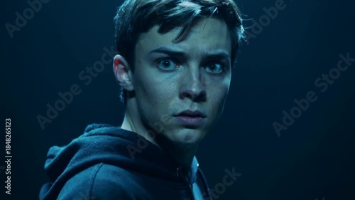 Young man looking fearful in dimly lit room with blue lighting  