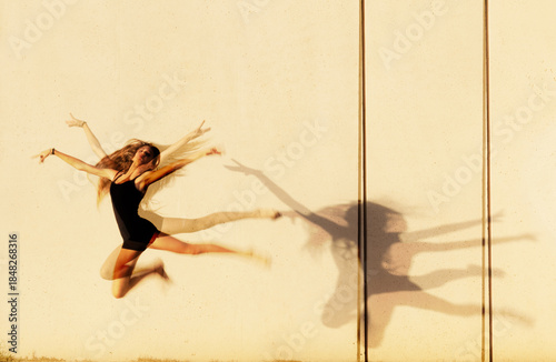 Artistic motion blur of a young girl leaping and dancing against a concrete wall