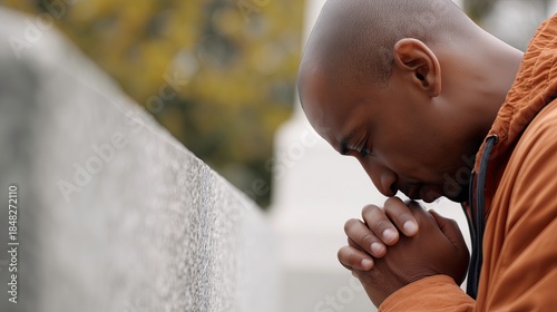 Black man praying silently at cemetery with bowed head  