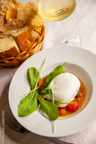 Italian cheese burrata with arugula and tomato close up and glass of white wine