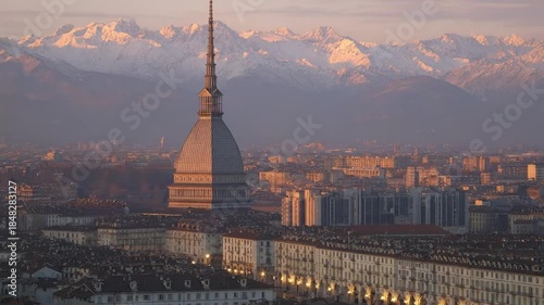 An breathtaking aerial panorama showcases a vast city at the golden hour, bathed in the soft, warm glow of sunrise or sunset. A magnificent, distinctive architectural tower rises prominently from the 