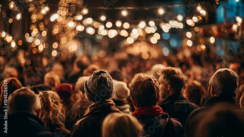 Crowd enjoying an outdoor gathering illuminated by warm string lights, creating a cozy and festive atmosphere. People are shoulder-to-shoulder