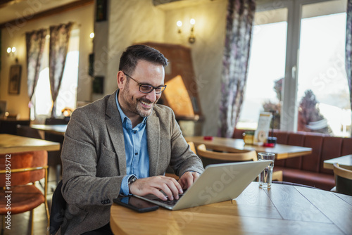 Foto Mature businessman working on laptop in cafe smiling happily