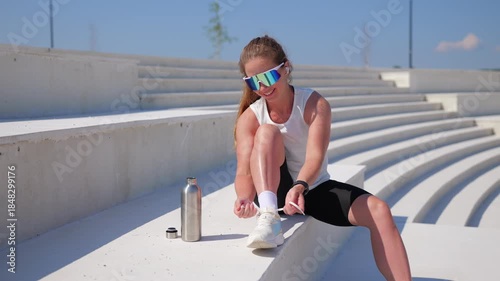 Woman sits on white steps tying her shoes and smiling