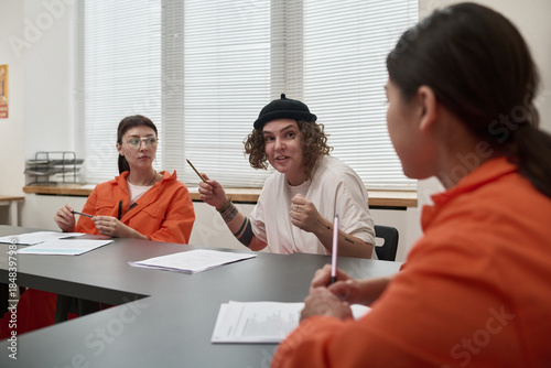 Fotografija Three young adult women sitting at table discussing educational materials in cla