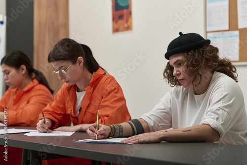 Konstfotografi Three young adult women sitting at desks writing on paper during prison educatio