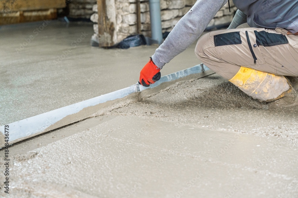 Naklejka premium A skilled craftsman levels a concrete floor with a hand trowel, ensuring a smooth surface. Ideal for illustrating construction, renovation, and home improvement projects.