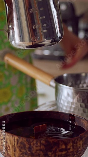 Vertical video. Woman Pouring Clear Melted Wax into Coconut Candle Bowl in Bright Kitchen Light with Careful Steady Motion, Handmade Craft Concept