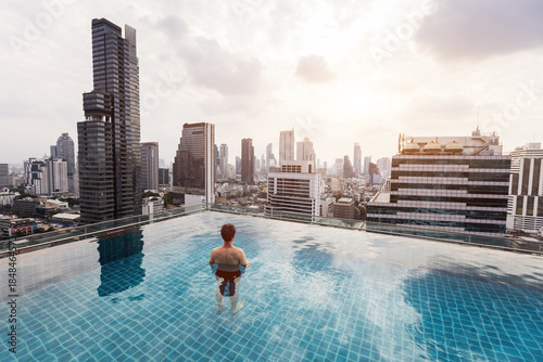 Photography man in rooftop infinity pool in Bangkok city, tourist relaxing in swimming pool