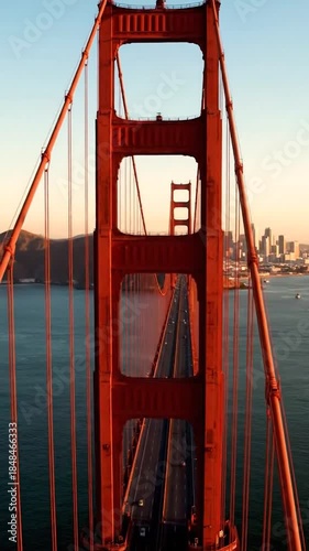 Aerial view through an iconic red bridge tower at sunset, city in background
