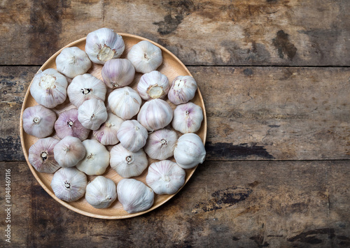 Top view of organic garlic bulbs in a wooden plate with copy space on rustic wood background.