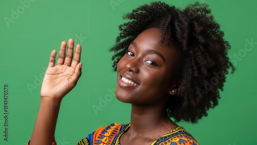 Portrait of a smiling young woman with natural afro hairstyle waving against a vibrant green