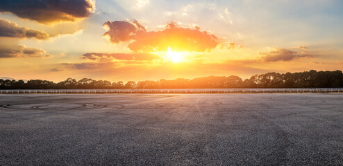 Empty asphalt race track and green forest with beautiful sky clouds landscape at dramatic golden sunset