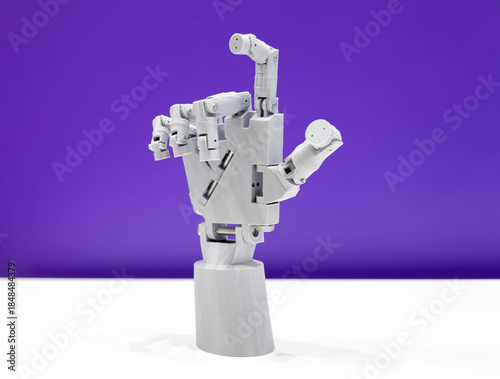 3D printed toy robot hand on white table purple wall