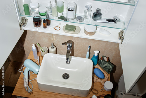 Slika na platnu Bathroom sink surrounded by various personal care products, electric hair dryer,