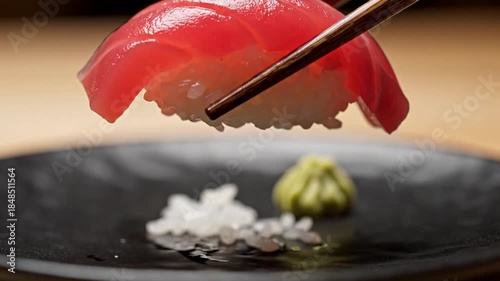 Sushi being delicately placed on a black plate with chopsticks