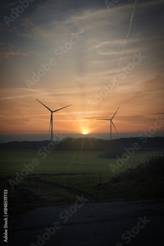 A scenic sunset over a rural landscape with wind turbines standing against a colorful evening sky.