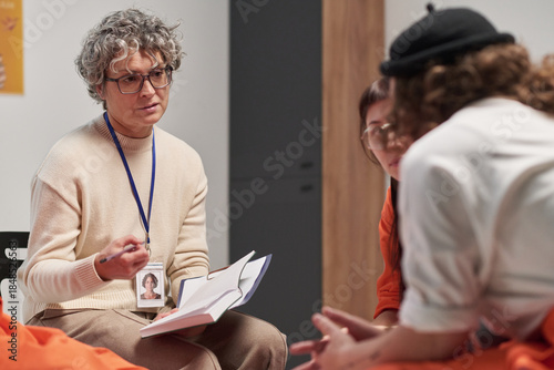 Tableau sur toile Middle aged Caucasian woman with curly gray hair holding open notebook, engaging