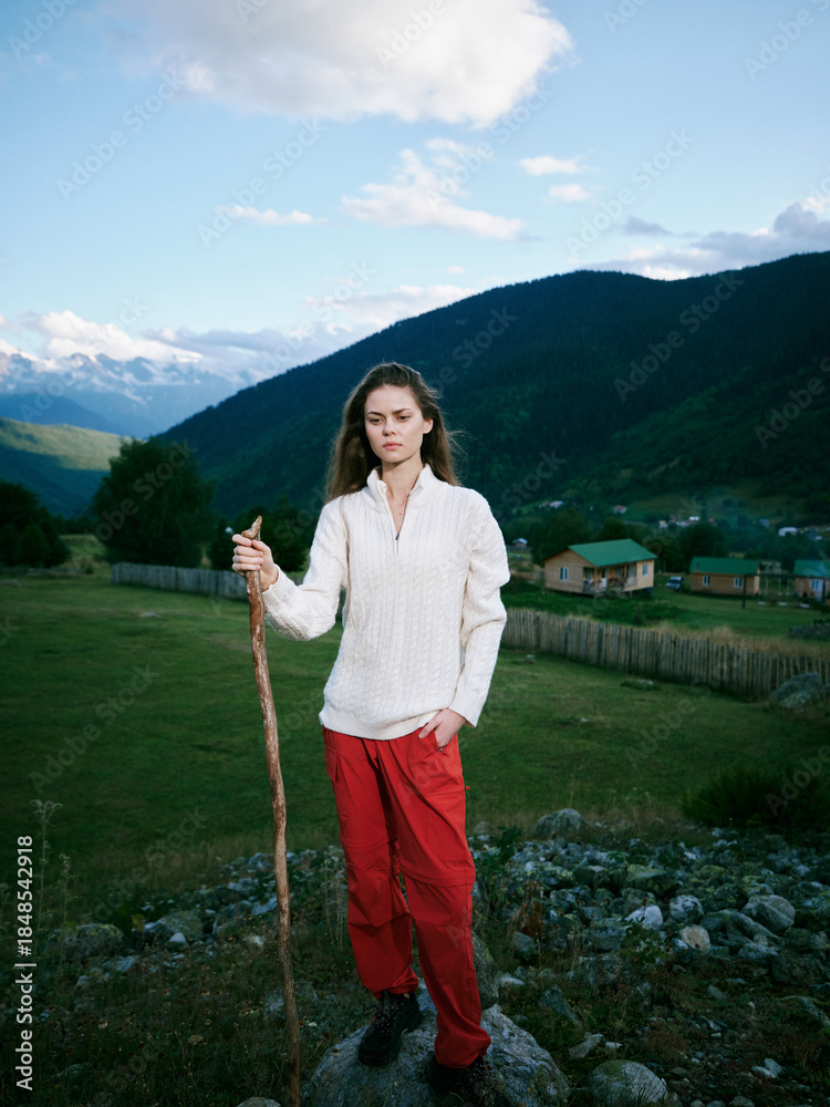 Fototapeta premium Nature, countryside, girl, hiking, outdoors, mountains, landscape, walking stick, rural, scenery describe a girl standing on rocky ground in a white knit shirt and red pants under a blue sky in wide