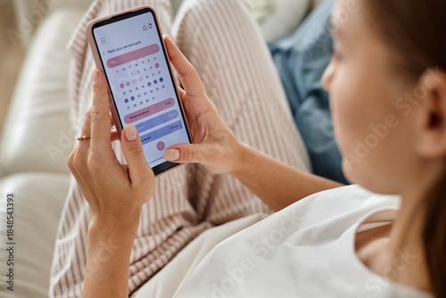 Bild auf Leinwand Caucasian young adult woman holding smartphone while checking menstrual cycle ca