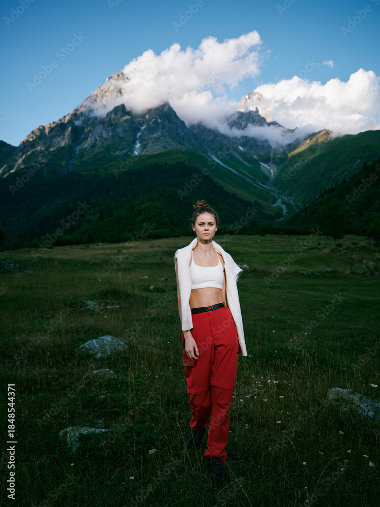 Naklejka premium Mountains, meadow, woman, outdoor fashion travel landscape nature adventure scenery in alpine valley with clouds and grass under a clear sky, stylish casual look and wild landscape mix