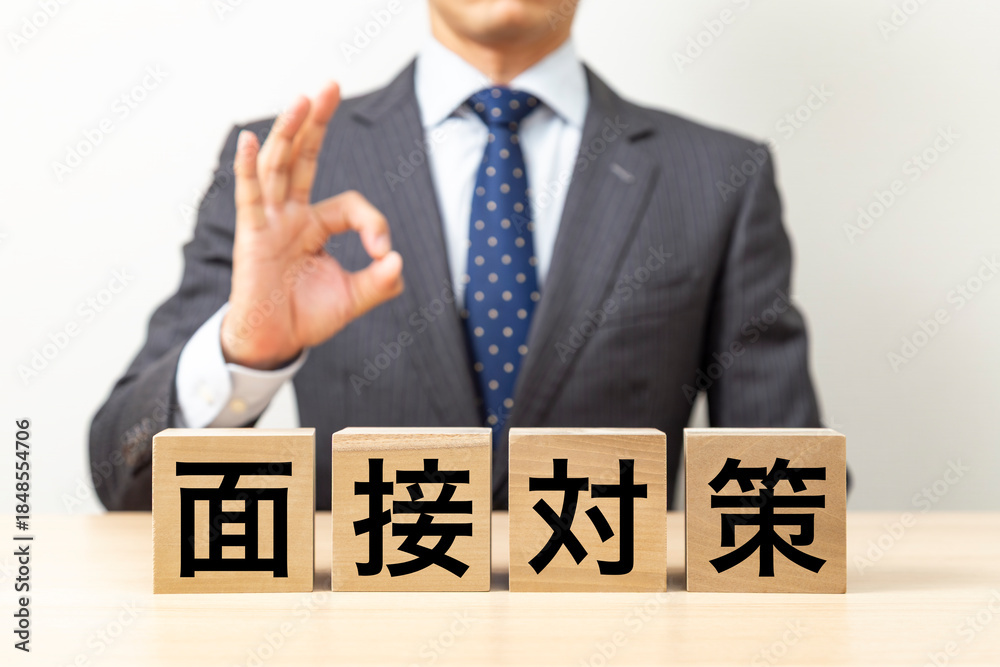 Obraz premium 「面接対策」と書かれたブロックとOKポーズをするビジネスマン