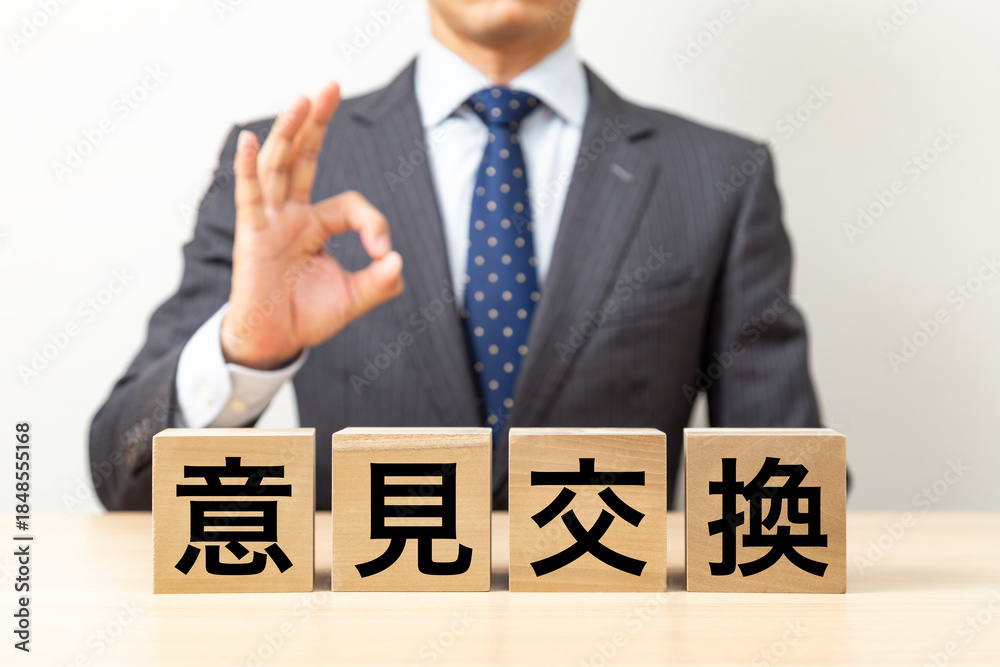 Obraz premium 「意見交換」と書かれたブロックとOKポーズをするビジネスマン