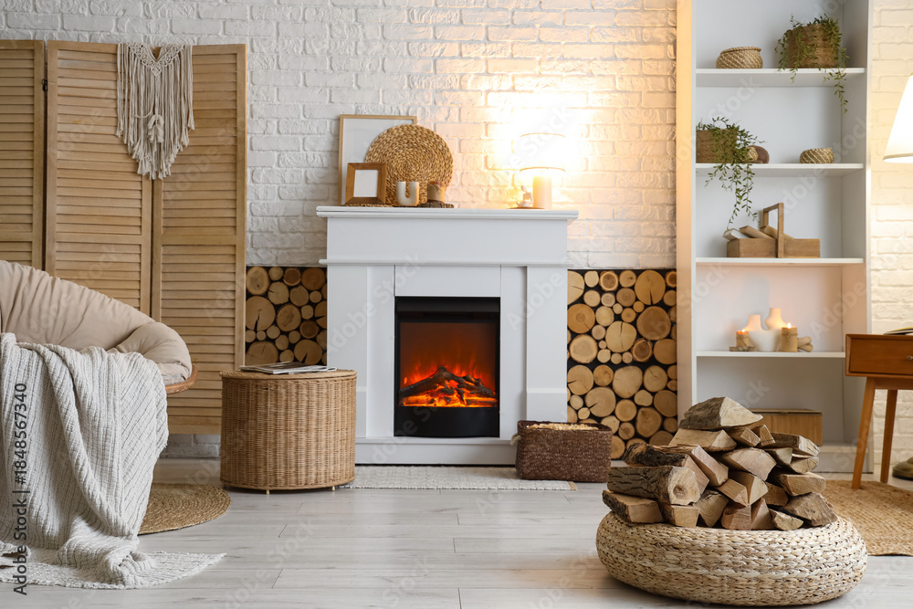 Fototapeta premium Interior of living room with armchair, shelving unit, folding screen, coffee table and firewood near fireplace