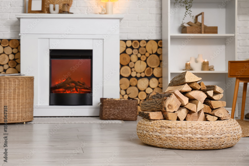 Fototapeta premium Interior of living room with shelving unit, wicker ottoman and firewood near fireplace