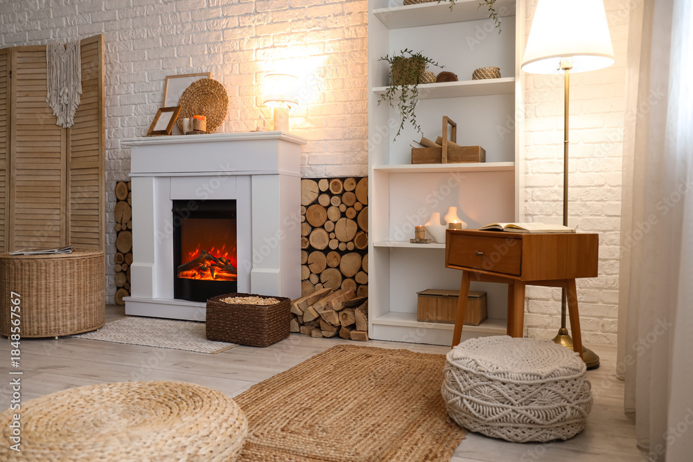 Fototapeta premium Interior of living room with shelving unit, folding screen, wicker coffee table and firewood near fireplace