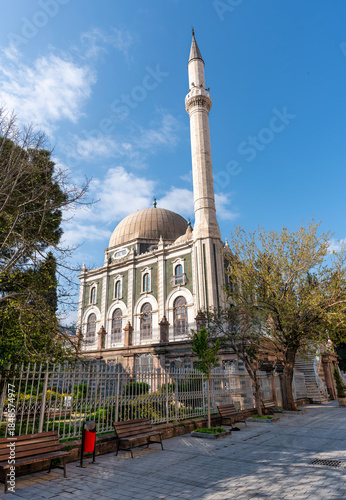 Salepcioglu Mosque, Izmir, Turkey. Historic mosque with its dome and minaret, surrounded by trees and a fence, under a bright blue sky.