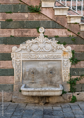 Ornate marble fountain with two spigots and basin on the stone wall of Salepcioglu Mosque, Izmir, Turkey. Historic architecture featuring carved details and natural stone blocks