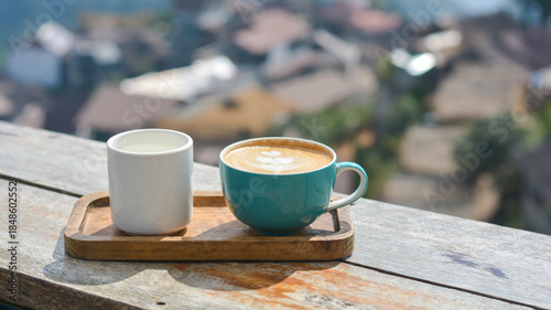 Hot cappuccino in a blue cup, served with hot water, on a wooden table and blurry nature background.