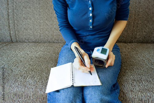 Картината върху платно Young woman holding a blood pressure monitor and writing health observations in a notebook