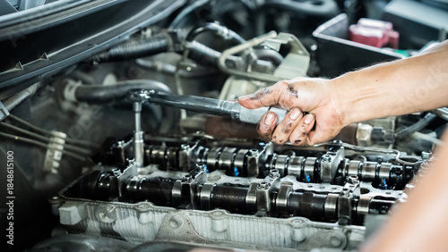 A mechanic is working on a car engine, using a wrench to loosen a bolt. Concept of manual labor and expertise, as the mechanic carefully manipulates the engine parts.
