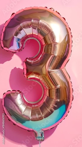 A shiny golden number three balloon with pink borders, casting a shadow on a pink background