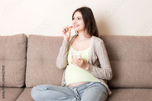 pregnant woman is sitting in sofa. Taking pills from colds. Last months of pregnancy