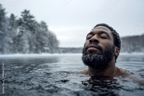 man practicing cold water immersion in icy winter lake surrounded by snow covered forest during serene meditation.