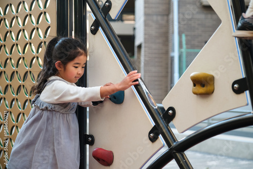 Japanese girl playing on playground climbing wall outdoors
