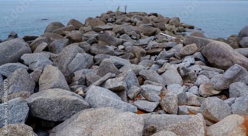 A rocky breakwater made of large granite stones extending into a calm tropical sea, creating a strong leading line and peaceful coastal atmosphere.