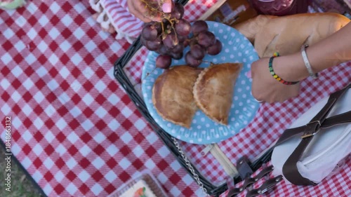 Top view of a mother serving grapes and bread on a plate at a picnic with a checkered tablecloth.